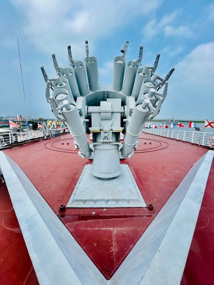 Detailed view of naval artillery system on a military ship deck under a blue sky.